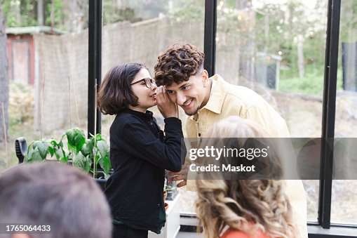 Boy whispering to young man at patio during party Boy whispering to young man at patio during party