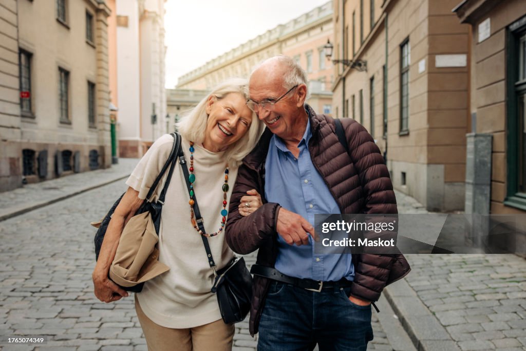 Happy retired senior couple with arm in arm strolling on city street