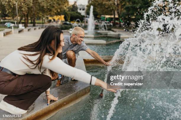 young man and young woman playing with water - fountain stock pictures, royalty-free photos & images