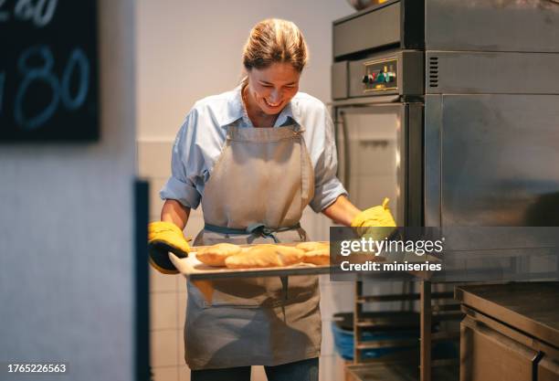 retrato de una mujer sonriente sosteniendo una bandeja de pan fresco en la panadería - panadería fotografías e imágenes de stock