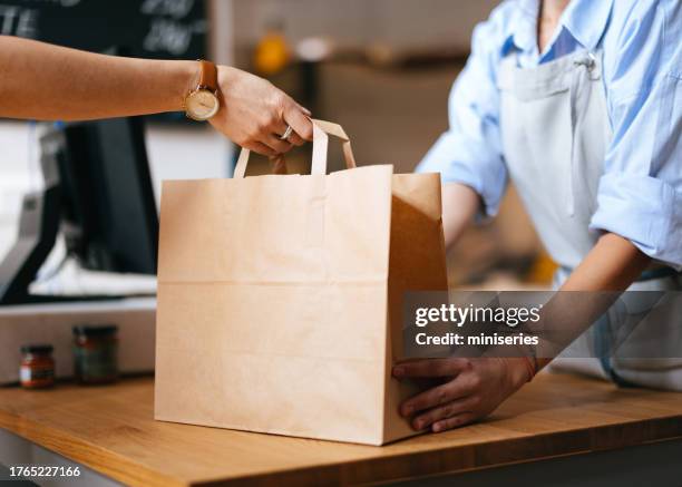 nicht erkennbare mitarbeiterin, die einem kunden eine verpackte bestellung gibt - papiertüte stock-fotos und bilder