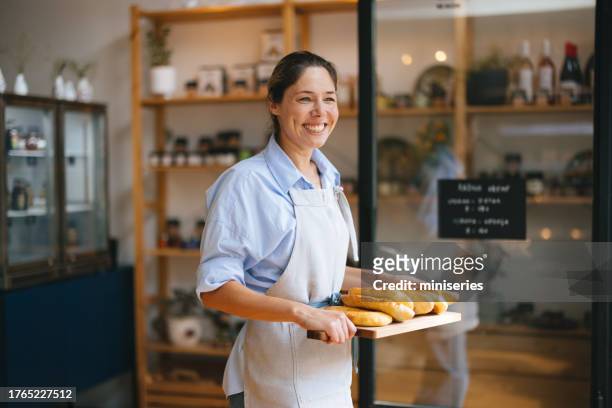 porträt einer schönen bäckerin, die ein tablett mit brotlaiben hält - bäckerin stock-fotos und bilder