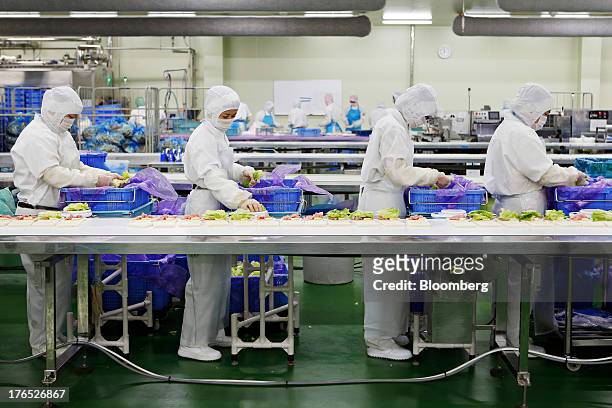 Employees weigh lettuce on scales before placing the leaves in the filling of ham-and-cheese sandwiches, for Seven & I Holdings Co.'s 7-Eleven...