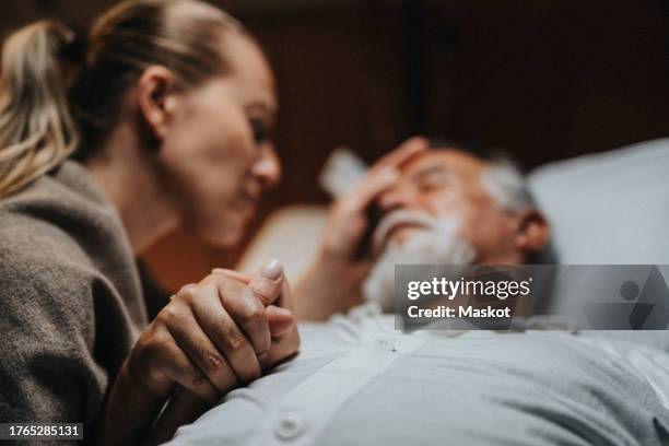 daughter holding hands of critical father in hospital ward - cuidados paliativos fotografías e imágenes de stock