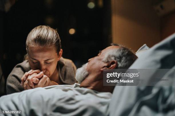 daughter kissing on hand of father lying down in hospital - ospizio foto e immagini stock