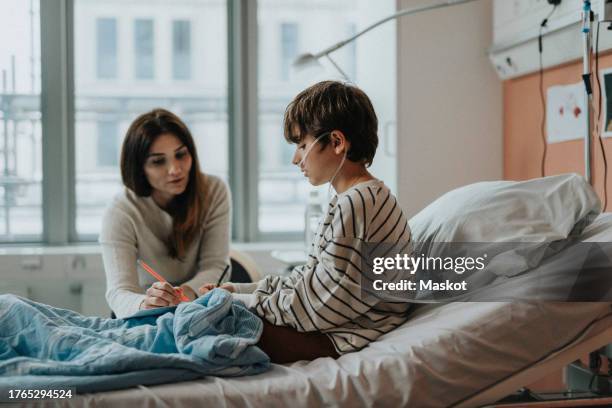 side view of son playing games with mother while sitting on bed in hospital - tubo de oxígeno fotografías e imágenes de stock