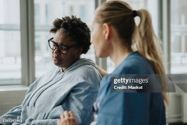 female nurse consoling sad patient sitting at hospital - black women crying stock pictures, royalty-free photos & images
