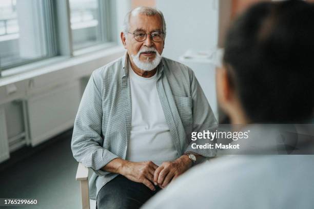 senior male patient sitting with doctor during consultation at hospital - male doctor man patient stock-fotos und bilder