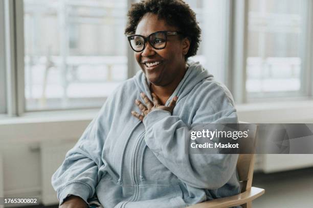 happy mature female patient sitting with hand on chest at healthcare center - hands on chest relief stock pictures, royalty-free photos & images
