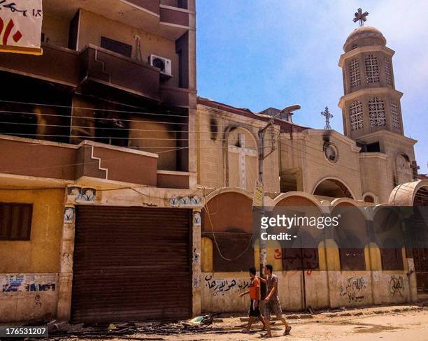 Two Egyptian youths walk past a church that was partially burnt after being torched by unknown assailants in the central Egyptian city of Minya on...