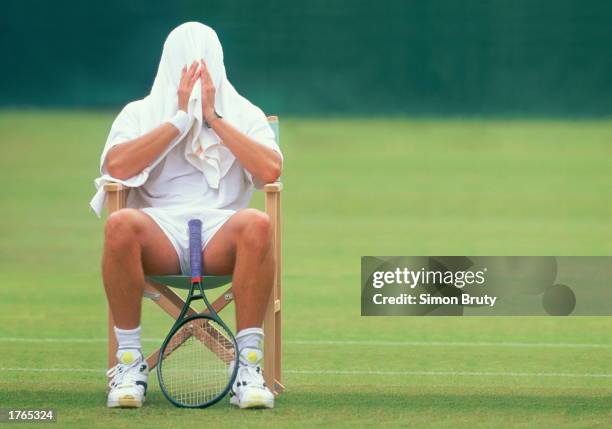 Tennis player resting between games, towel covering head