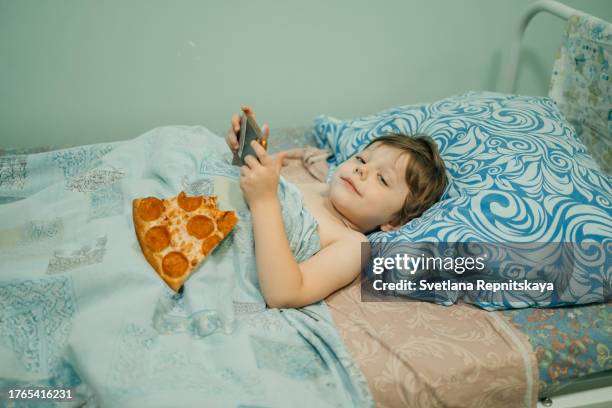 child eating pizza after surgery while lying on bed in hospital - hernia recovery stock pictures, royalty-free photos & images