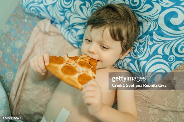 child eating pizza after surgery while lying on bed in hospital - hernia recovery stock pictures, royalty-free photos & images