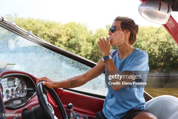 mid adult confidence woman steering boat wheel and smoking electronic cigarette - adrenaline junkie stock pictures, royalty-free photos & images