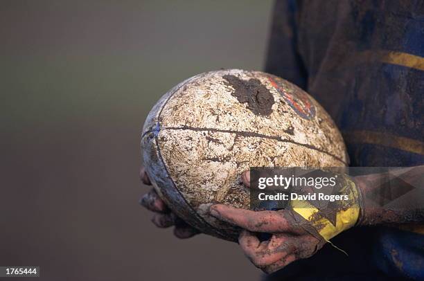 Rugby, player''s mud-covered hands holding ball, close-up