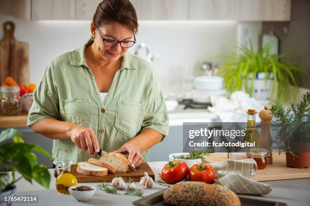 retrato de una mujer madura rebanando pan - carbohidrato fotografías e imágenes de stock