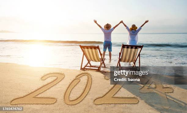 couple standing on new year number 2024 beach with arms raised - new year 2018 stock pictures, royalty-free photos & images