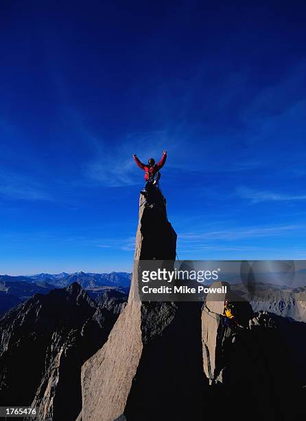 Male climber sitting on top of pinnacle, arms raised