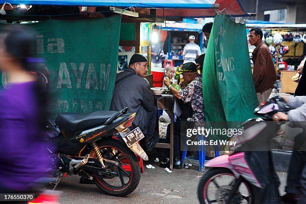 People eat dinner at a roadside stand on a busy road on August 15, 2013 in Jakarta, Indonesia. Street vendors use any available space to sell their...