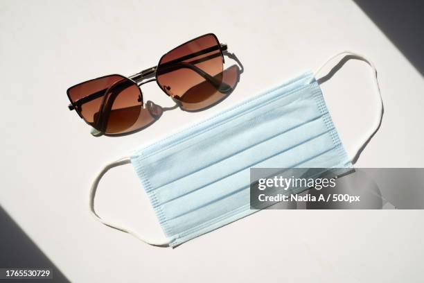 dark sunglasses and a blue face mask against white background with copy space - editorial template stock pictures, royalty-free photos & images