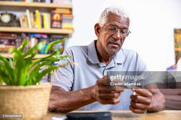 senior black man checking blood glucose sugar levels on finger at home - risk meter stock pictures, royalty-free photos & images