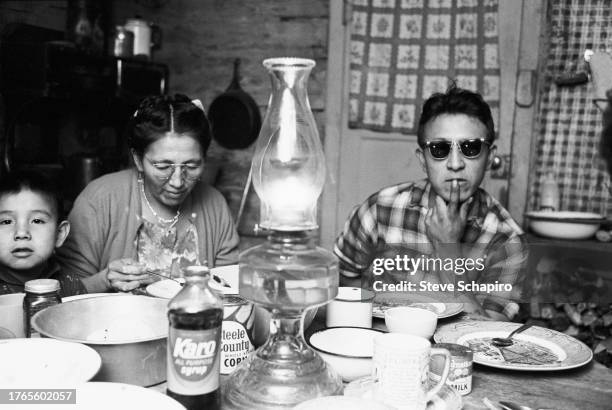 View of the unidentified members of a family as they eat a meal at a table in their home on the Oglala Lakota people's Pine Ridge Indian Reservation,...