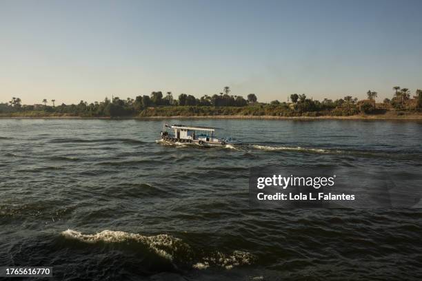 boat crossing the nile river at sunset, on the way to assuan, egypt - rivier gras oever stockfoto's en -beelden