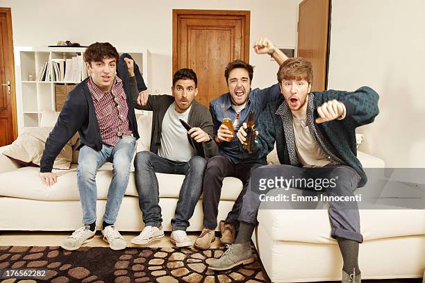 young men watching tv indoors exulting - four people foto e immagini stock