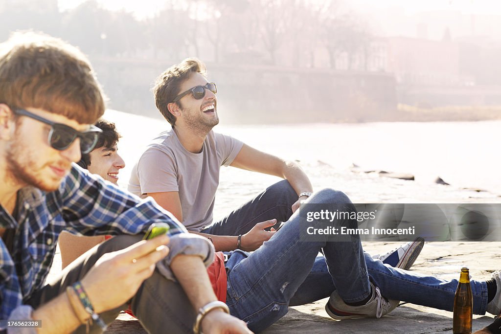 Group of friends, sitting by river, beer, phone