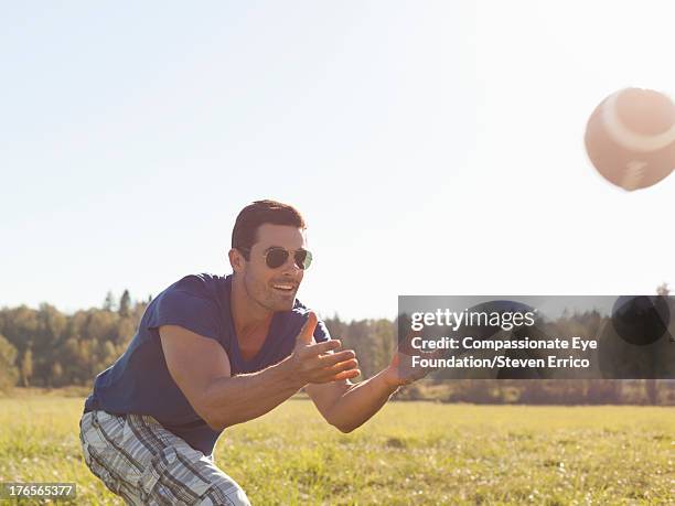smiling man catching football in field - eye catching stock pictures, royalty-free photos & images