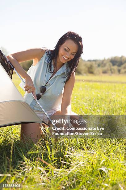 smiling woman putting up tent outdoors - camisa sin mangas fotografías e imágenes de stock