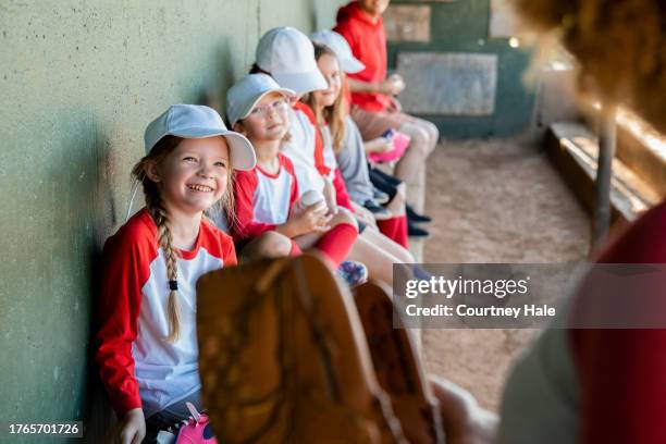 seated in the dugout are six elementary school-aged children, all sporting baseball team uniforms - softball stockfoto's en -beelden