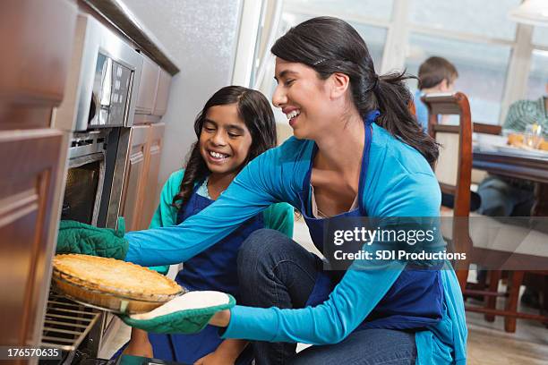 mom and daughter removing apple pie from oven in kitchen - hot latino girl stock pictures, royalty-free photos & images
