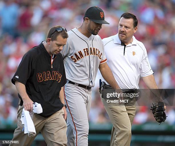 San Francisco Giants relief pitcher Sandy Rosario walks off the field with San Francisco Giants trainers Mark Gruesbeck, left and Dave Groeschner...