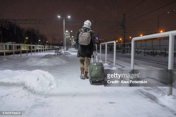 on a cold, snowy night in the winter, a woman with luggage walks away on a railroad platform. - alex potemkin coronavirus stock pictures, royalty-free photos & images