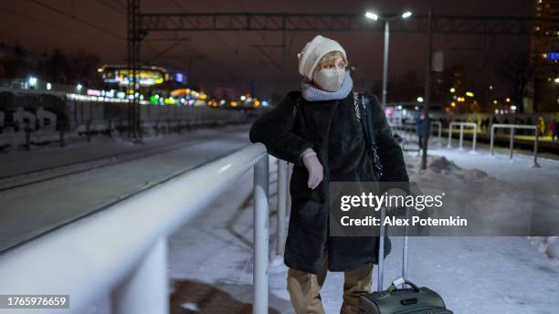 travel in winter. in the winter cold, snowy night, a mature woman with luggage waits on a railroad platform for a train. - coronavirus winter bildbanksfoton och bilder