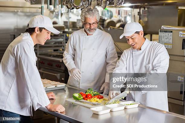 cooking instructor teaching culinary students in commercial kitchen - young chefs cooking stock pictures, royalty-free photos & images