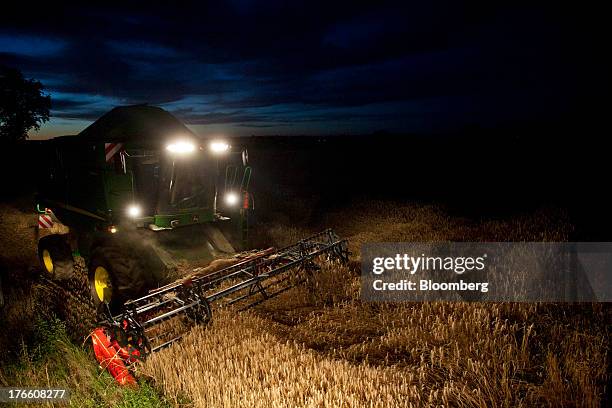 Headlights illuminate a field as a Deere & Co. John Deere W540 combine harvester gathers crops in a field of triticale wheat, in Falguieres,...