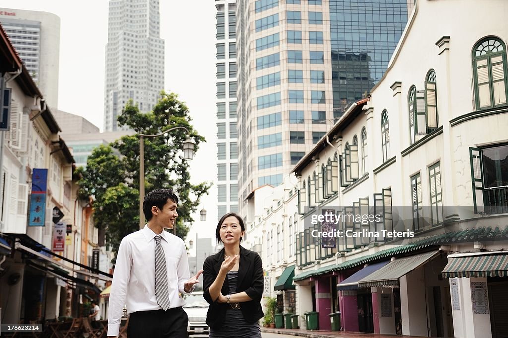 Two colleagues walk down a street with shop houses