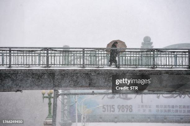 Person walks with an umbrella during snowfall in Harbin, in China's northeastern Heilongjiang province on November 6, 2023. / China OUT