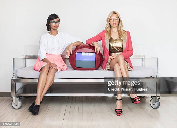 two stylish young women sitting on couch with tv - legs crossed at knee stock pictures, royalty-free photos & images