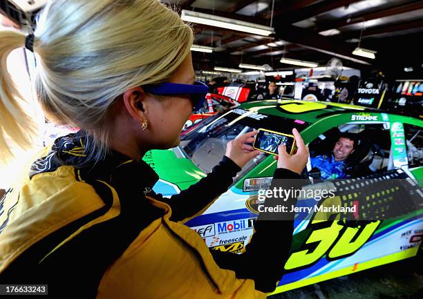 Miss Sprint Cup Brooke Werner takes a picture of David Stremme, driver of the Lean1 Toyota, sitting in his car in the garage during practice for the...