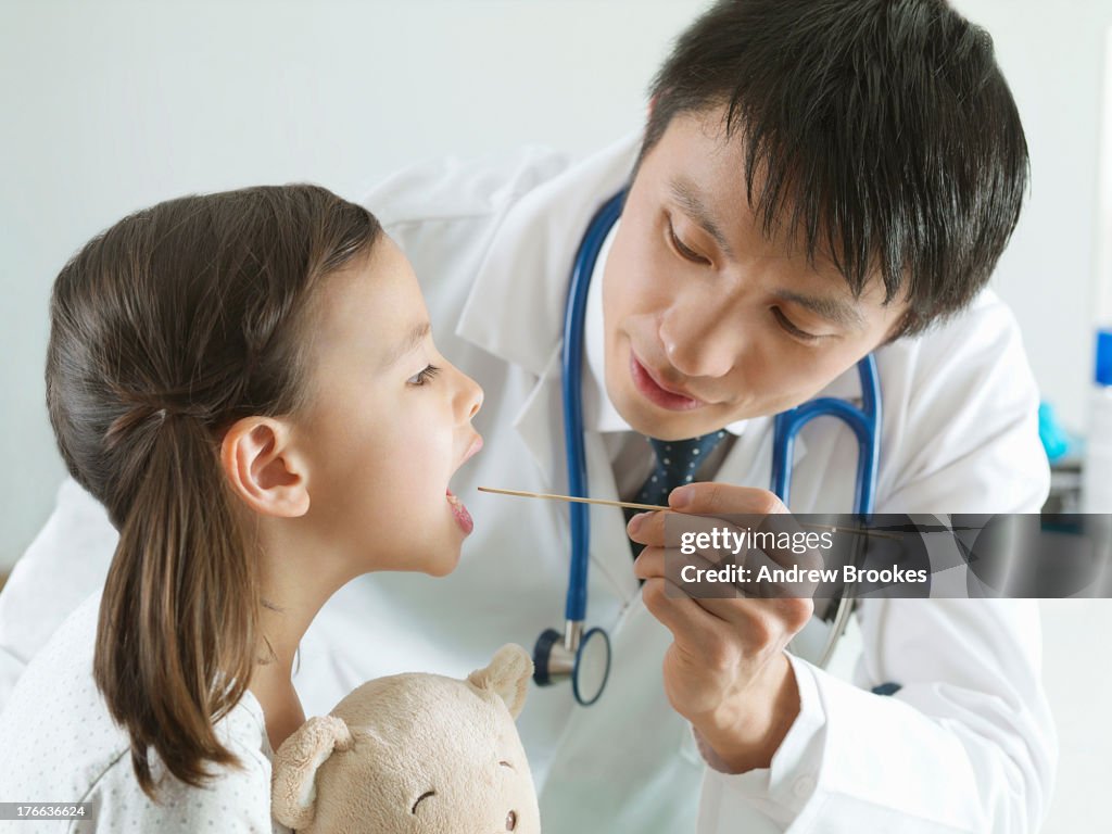 Paediatric doctor using tongue depressor on girl in examination room