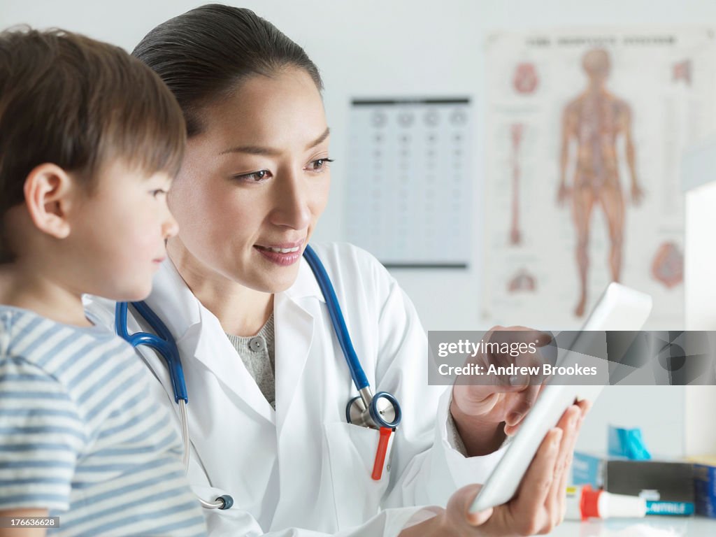 Paediatric doctor using digital tablet with child patient in  examination room