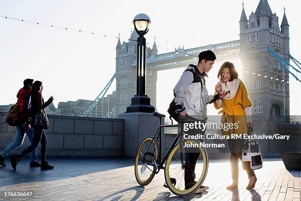 young man holding bicycle with woman at tower bridge, london, england - couple london stockfoto's en -beelden