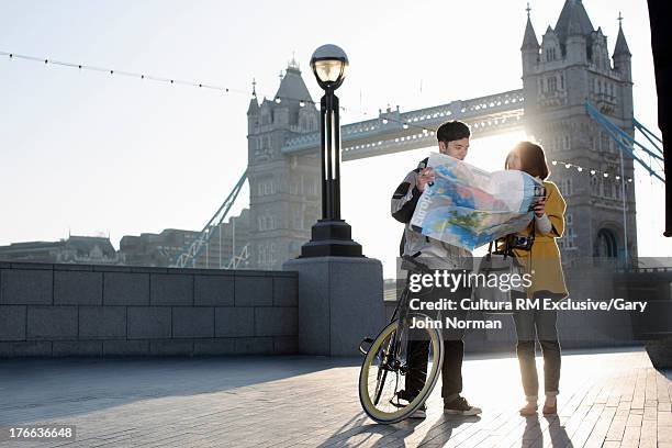 young couple reading map by tower bridge, london, england - london tower bridge fotografías e imágenes de stock