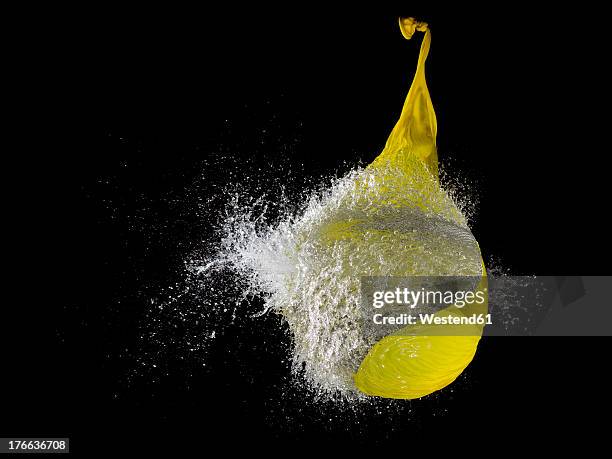 yellow waterballoon bursting against black background, close up - blowing up balloon stock pictures, royalty-free photos & images