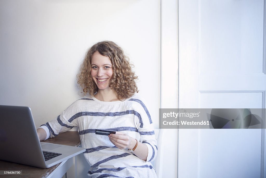Germany, Bavaria, Munich, Young woman shopping online from home with laptop and credit card
