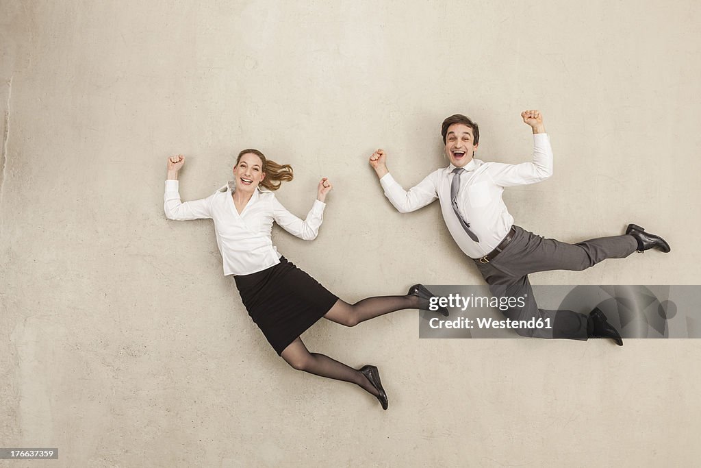 Businessman and businesswoman flying against beige background