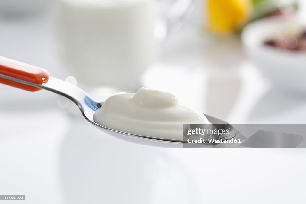 Spoon of yogurt against white background, close up